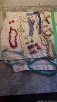 Overview of lot showing multiple bracelets, necklaces, and earrings on white towel on counter.