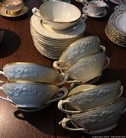 Photo showing 6 white ceramic soup bowls with two handles and raised floral patterns. Gold rims are intact.