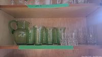 Shelf view of green glassware set including pitcher, six water glasses, four juice glasses, and four crystal clear water glasses.