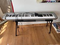 Full view of the Technics SX-P50 keyboard on black metal stand with attached cables and foot pedal laid on keyboard.