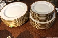 Stacks of three sizes of white porcelain Limoges T&V plates with gold trim, displayed in three piles showing sizes and quantity.