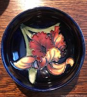 Top view of small circular Moorcroft dish showing dark blue gloss and raised multicolored floral decoration
