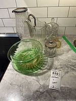 Full view of all items on countertop, showing two pitchers, green bowls and plates, sugar bowls, and creamer.