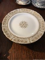 Close up of front of a plate showing gold ornate pattern around scalloped edge and central medallion