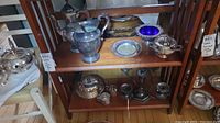 Shelf with silver-plated candelabra, teapot, pitcher, plates and candy dish with blue glass liner