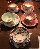 Overview of all five teacup and saucer sets on wooden table