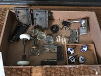 Full view of contents inside cardboard box with vintage door hardware and knobs laid out showing porcelain and glass knobs, metal lock plates, screws, and lever handle