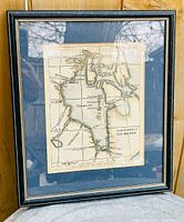 Frontal view of the framed antique map inside a black frame with gold trim, matte and glass covering, mounted on wooden panel.