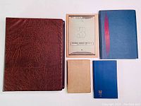 Photo of all five items: 1 large brown textured leather album, 1 large blue cloth album with red stripes, 1 beige album, 1 smaller blue album with gold crown, and 1 vintage paper booklet from Czechoslovakia.