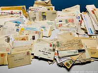 Photo showing large quantity of white and cream envelopes with stamps and postal markings, some airmail envelopes with red and blue borders.