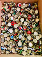 Close-up image showing a large quantity of vintage beer caps with varied designs and colors inside a box.