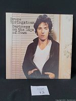 Front cover of Bruce Springsteen Darkness on the Edge of Town vinyl LP showing the artist in a leather jacket in front of blinds and floral wallpaper