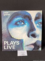 Front cover of the Peter Gabriel Plays Live vinyl record album showing painted close-up face photo and title text