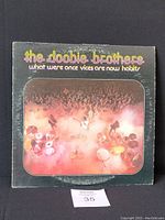 Front cover of The Doobie Brothers vinyl album 'What Were Once Vices Are Now Habits' showing stage and crowd scene, with title and band name in colorful fonts on black background.