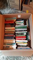 Box filled with assorted books of various colors and sizes, arranged horiztonally and vertically.