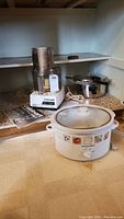 Photo of kitchen shelf showing Cuisinart food processor, Proctor Silex slow cooker, and Presto pressure cooker together.