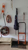 Suncoast hose reel with hose coiled on reel, hanging aprons, hanging trouble lamp with protective cage and cord, and convertible light duty dolly with orange and black frame.