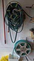 First photo showing two wall mounted hose reels, larger black reel with green hose with orange nozzle above a smaller plastic light green and white hose reel with green hose.
