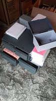 Six gray metal index card boxes on a carpet beside a cardboard box, some drawers open showing assorted index cards and dividers inside. Additional index cards stacked on top and beside the boxes.