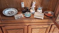 Wide view showing all items on wooden cabinet including plates, boxes, sewing machine, figurine, and snow globe.