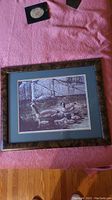 Full view of the framed print showing geese and goslings by a rocky water area, brown textured frame and green mat.