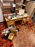 Overview of wooden desk with drawers and multiple clipboards, electronic devices, and office supplies spread out on and around the desk