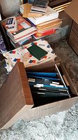 Full view showing cardboard file box filled with hanging folders and surrounding paper supplies, envelopes, and storage boxes.