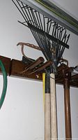 Metal garden and leaf rakes hanging with a hand saw, wooden handled