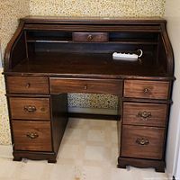 Front view of vintage wooden roll top desk showing drawers, cubby compartments, and worn dark wood finish.