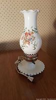 Full image of one vintage lantern-style table lamp showing white milk glass base with beaded edge, floral and number painted glass shade, metal holder with winding key, power cord and plug.