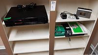 Three shelf white shelving unit with Sony CD player on left, Hanimex Hanorama and Realistic scanner on right shelf, power cords and manuals on shelf.