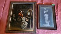 Two framed vintage prints laid out on pink fabric: a painting of a seated woman artist and a black and white photograph of Venus de Milo statue