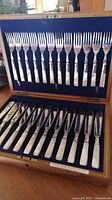Top view of the set showing 12 silverplate fish forks with mother of pearl handles arranged vertically within a lined wooden presentation case.