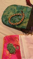 Amber-colored stone bracelet on a green pouch with gold dragon and floral patterns.