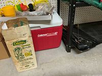 Photo showing Coleman PolyLite 40 cooler, original Coleman Model 200 lantern box with graphics, and black mallet on floor.