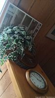Photo of potted faux ivy plant alongside two round wooden frame clocks on a wooden surface