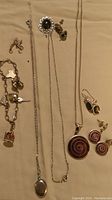 Full view of charm bracelet, several necklaces including locket, spiral pendant, and matching spiraled earrings and black stone earrings.