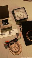 Photo shows various jewelry items laid out including boxed rhinestone necklace and earrings, roses gold mesh bracelet, Joan Rivers marked black pouch with bangle, and paper tag.