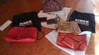 Photo showing six leather handbags and wallets arranged on floor with storage dust bags, brand logos visible including Aimee Kestenberg and Maxx New York.