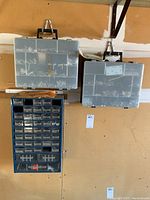 Wide view showing two portable translucent plastic hardware organizers hanging on wall above a blue metal multi-drawer hardware storage unit mounted on the wall.