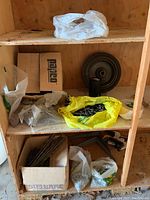 Shelf with multiple bags and boxes containing various hardware including screws, nails, and metal spikes distributed loosely.