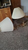 Two lamps lying on carpeted floor with matching pleated white conical shades; brass-colored metal bases. Shows adjustable table lamp and wall-mounted lamp.