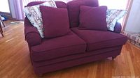 Front view of burgundy La-Z-Boy loveseat with four cushions on a hardwood floor.