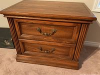 Front angle photo showing two drawers with metal handles, decorative framed panels, vertical fluted sides, and wood grain finish.