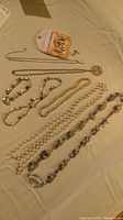 Multiple pearl and pearl-like necklaces, bracelets, earrings laid out on tan fabric, showing full set and pouch.