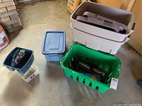 View showing two large beige Rubbermaid storage totes stacked with lids, a green grocery-style tote, and a smaller blue plastic tote with lid.