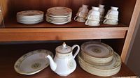 Full view of dishes including stacked plates, saucers, teacups, serving bowl, and teapot showing pattern and quantity.