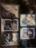 Photo of six NBA basketball cards featuring Ja Morant and Anthony Edwards in protective sleeves on a dark marble surface.