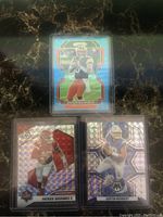 Front view of three NFL quarterback football trading cards featuring Baker Mayfield, Patrick Mahomes II, and Justin Herbert. Cards are in clear protective sleeves with mosaic and prizm holographic patterns.