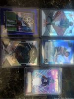 Top-down view of 4 NFL rookie football cards including DeVonta Smith, Alvin Kamara, and Ja'Marr Chase in protective sleeves on a dark surface.